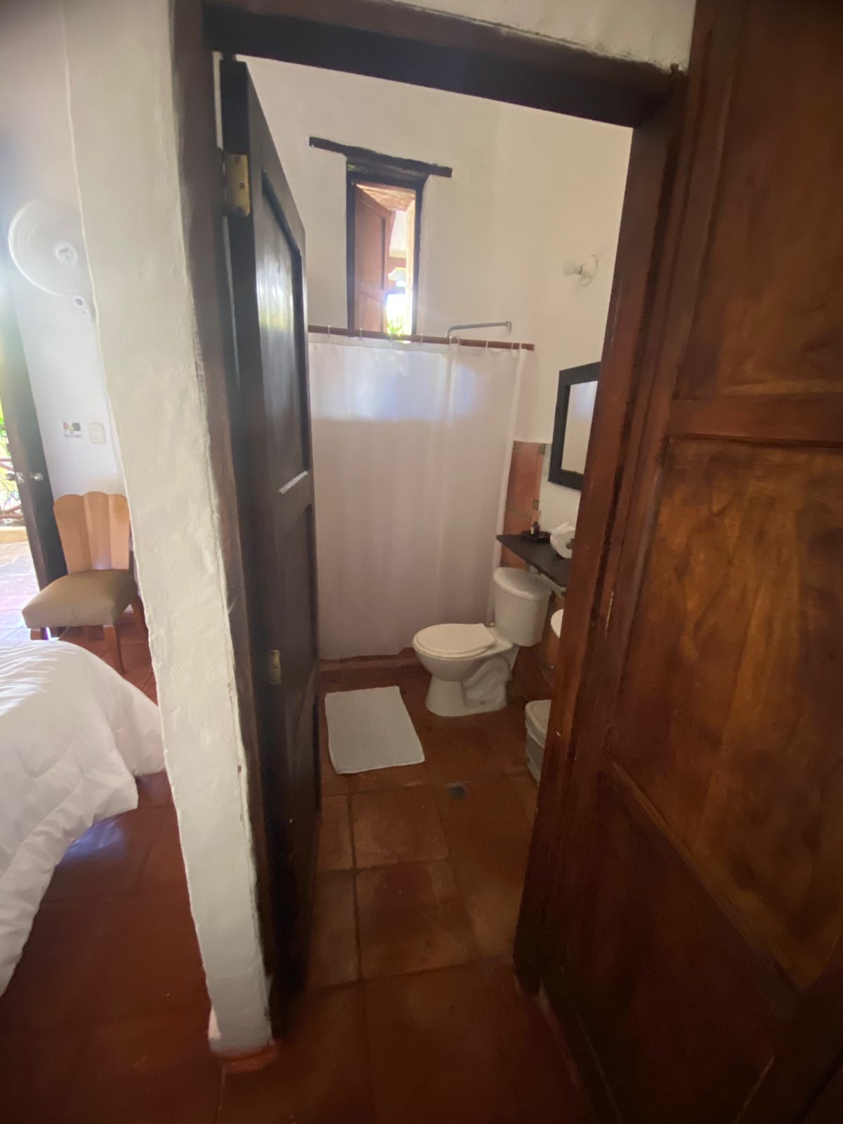 Baño privado con ducha, lavamanos y ventana de madera al corredor.