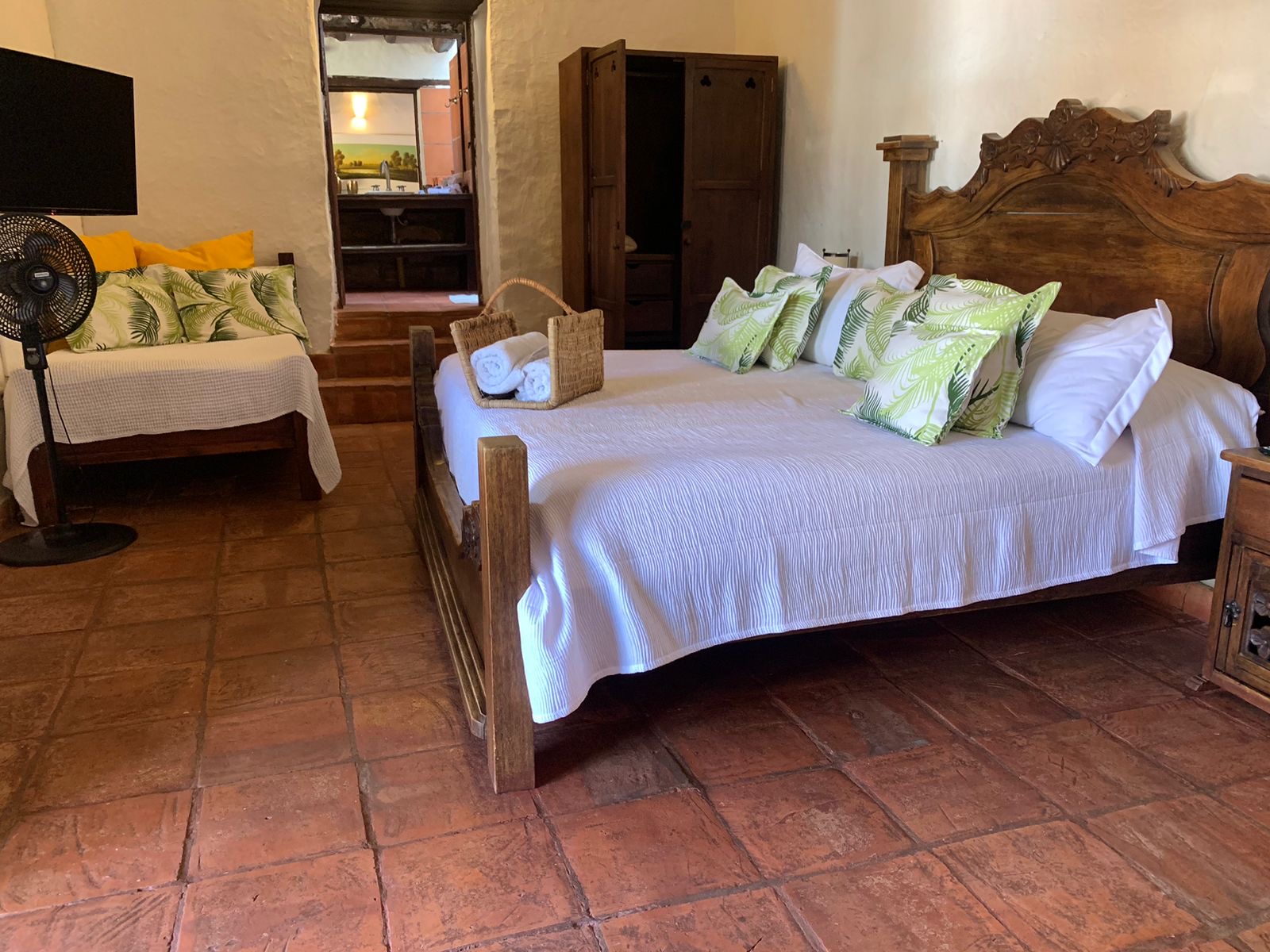 Habitación amplia con cama king de cabecero tallado y una cama auxiliar, y el baño subiendo unos escalones.