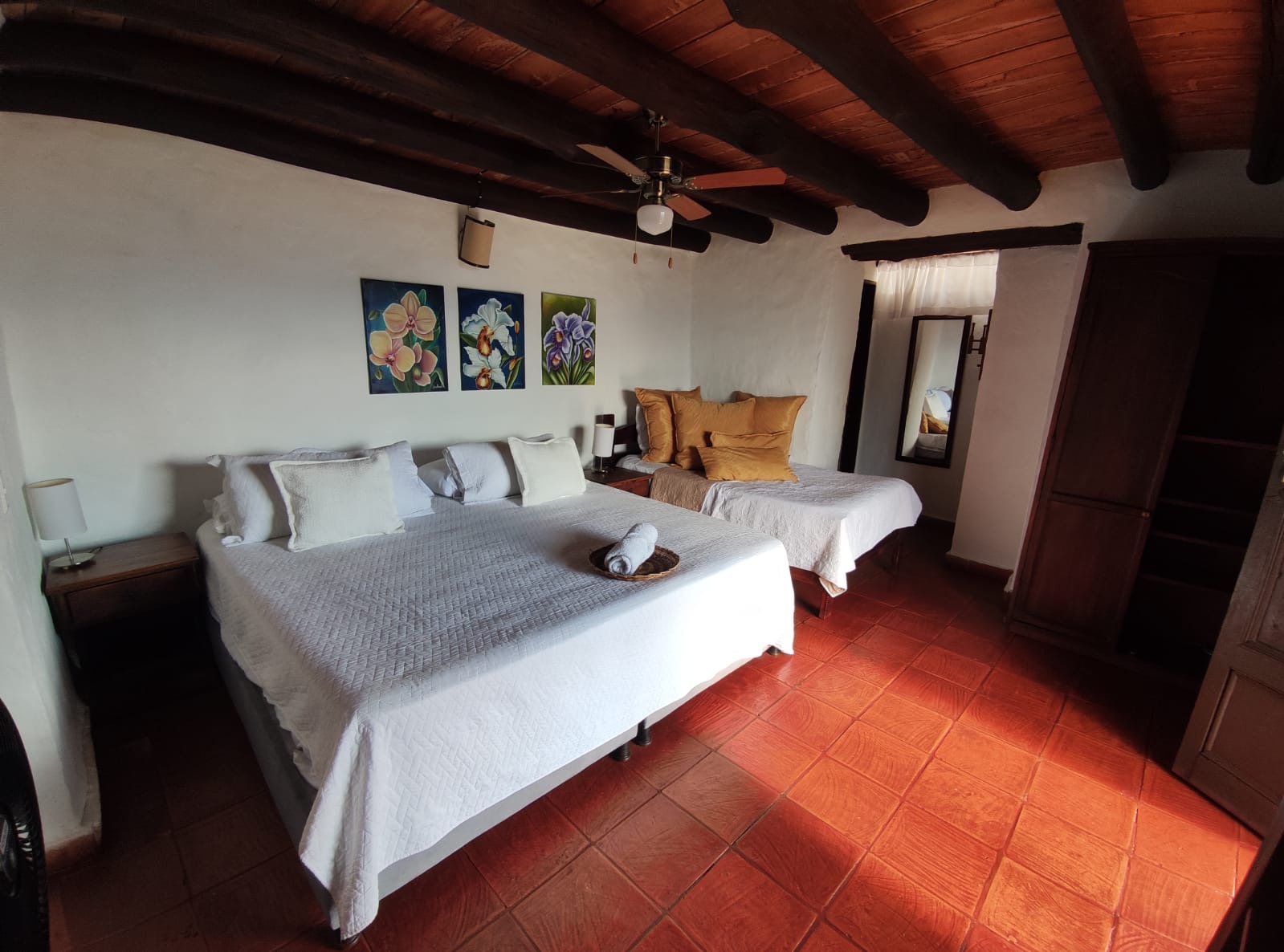 La misma habitación vista completa: techo de vigas de madera, ventilador y armario de madera maciza.