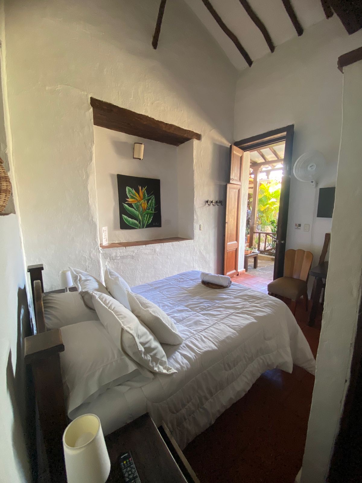 Habitación con cama doble y puerta abierta al corredor con plantas.