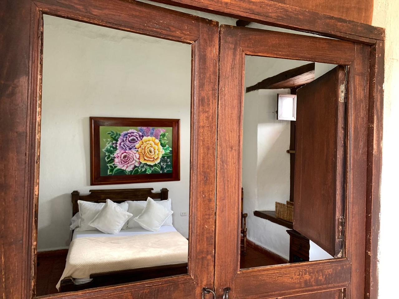 Ventana interior de madera antigua que enmarca una habitación y un cuadro de flores.