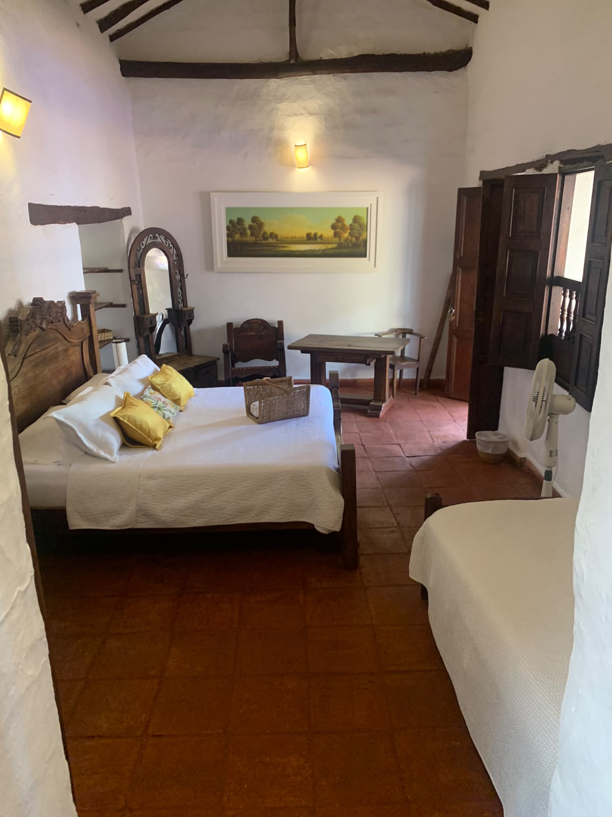 Habitación con cama doble y cama sencilla, vigas de madera a la vista y piso de baldosa de barro.
