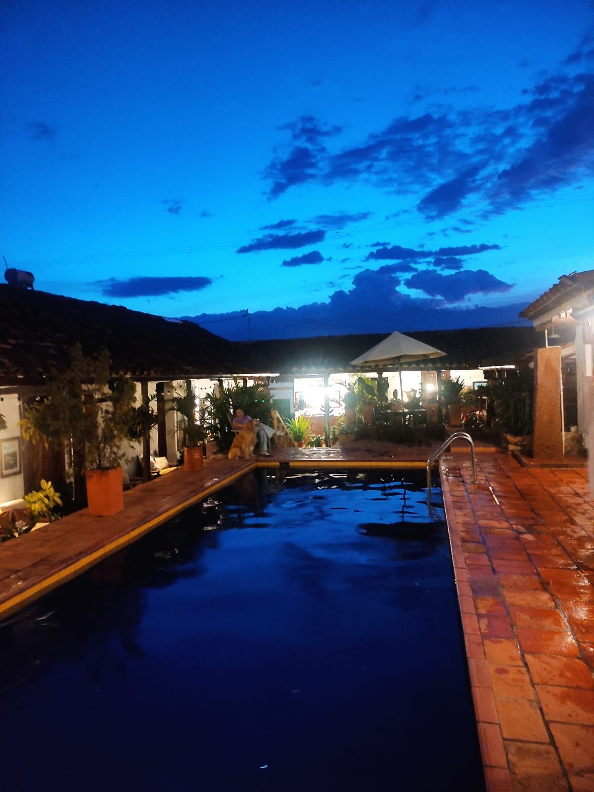 La piscina al anochecer, con el cielo azul profundo y las luces del corredor encendidas.